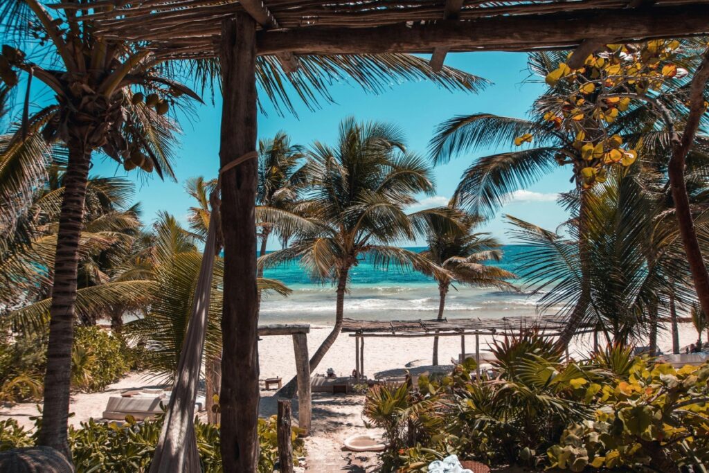 Esta imagen presenta una idílica playa mexicana, con palmeras ondeando suavemente bajo un cielo azul intenso. El mar de tonos turquesas se funde con la arena blanca, y estructuras de madera, como toldos y hamacas, ofrecen un lugar de relajación. En el contexto de "Pinterest México Cómo Usar Imágenes para Impulsar Tu Marca", si tu marca está vinculada al turismo, la ropa de playa, o los servicios de bienestar, imágenes como ésta pueden ser muy efectivas. Compartiendo en Pinterest y agregando hashtags como #PlayaMexicana, #TurismoRelajante y #MarCaribeño, puedes atraer a usuarios interesados y impulsar tu marca, mostrando la esencia del lujo y la relajación en México.